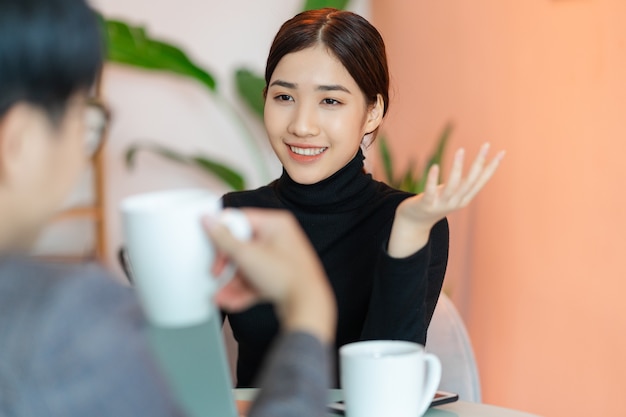 Asiatische Frau sitzt und plaudert mit Kollegen im Café nach der Arbeit