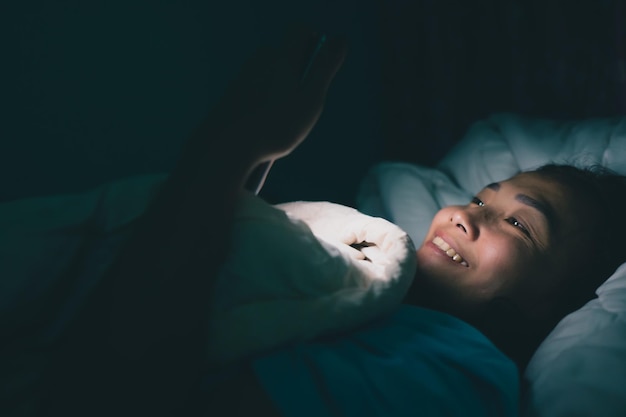 Asiatische Frau spielt nachts Smartphone im Bett