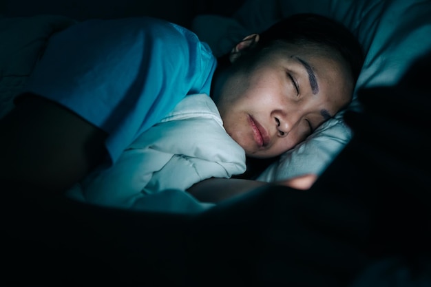 Asiatische Frau spielt nachts Smartphone im Bett