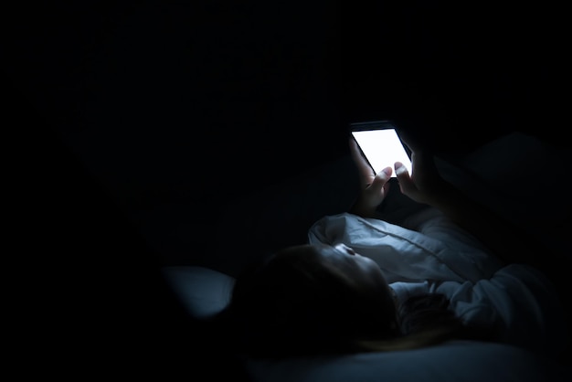 Asiatische Frau spielt nachts Smartphone im BettThailänderSüchtige Gesellschaft