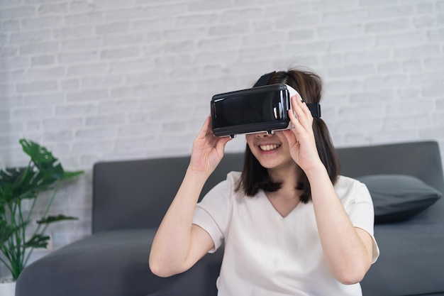 Asiatische Frau spielt VR-Spiel, um zu Hause zu unterhalten asiatische Frau, die im Urlaub im Haus fröhlich ist Glückliche Frau, die Metaverse VR-Technologiekonzept spielt