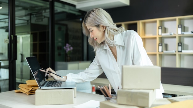 Asiatische Frau Startup Kleinunternehmer freiberuflich tätig Junges erfolgreiches Geschäft Asiatische Frau Online-Marketing-Verpackungsbox und Lieferung überprüfen Online-Bestellungen, um die Box vorzubereiten, die das Produkt verkauft