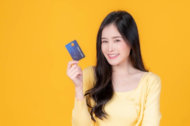 Asiatische Frau süßes Mädchen zeigt Kreditkarte für Online-Shopping und Zahlung per Kreditkarte isoliert auf gelbem Online-Shopping-E-Commerce-Telemarketing-Konzept