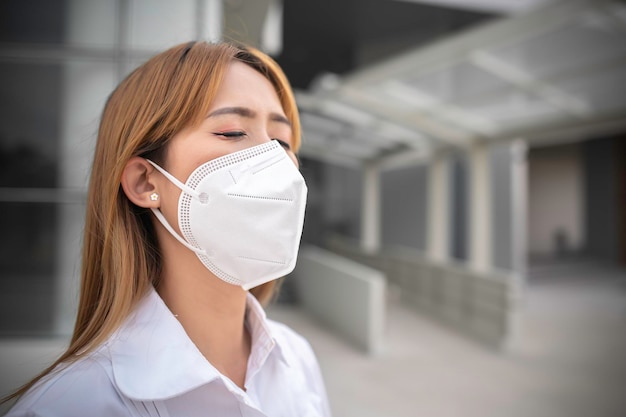 Asiatische Frau trägt eine N95-Maske zum Schutz von Staub pm 25Ökologiekonzept Allergie-Kopfschmerzen-Luftgefahr in der Stadt