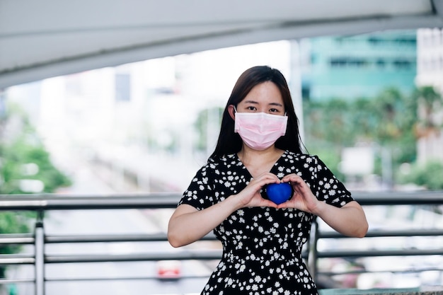 Asiatische Frau trägt Maske und hält blauen Ball in ihren Händen. Coronavirus-Konzept