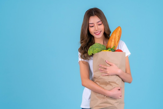 Asiatische Frau trägt Papiereinkaufstüte aus dem Supermarkt mit Gemüse in einer Tüte mit isoliertem