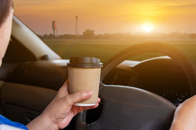 Asiatische Frau trinkt heißen Kaffee zum Mitnehmen in einem Auto und während der Fahrt mit dem Auto morgens während der Fahrt