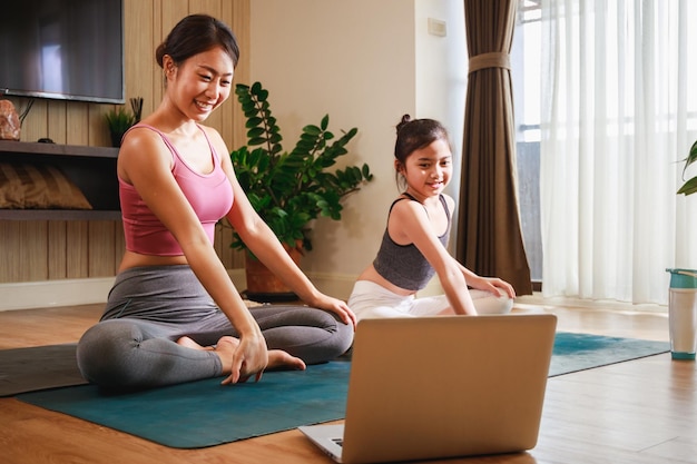 Asiatische Frau und kleines Mädchen praktizieren Yoga aus dem Yoga-Online-Kurs über Laptop zu Hause