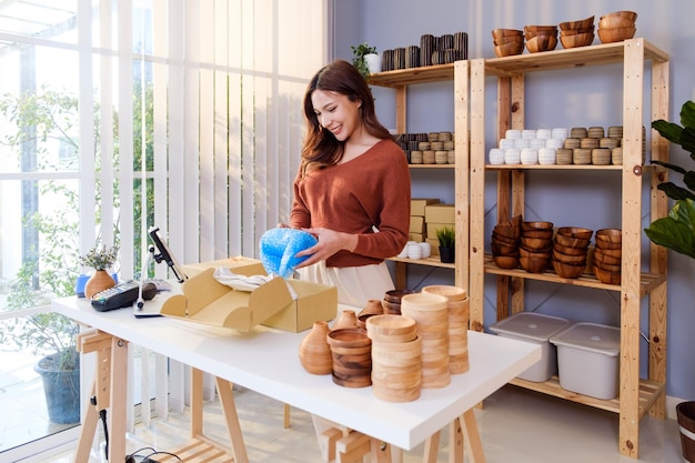 Asiatische Frau verpackt eine Vase mit Luftpolsterfolie für ein zerbrechliches Produkt, bevor sie das Paket verschickt