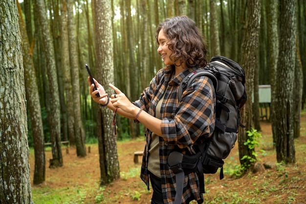 Asiatische Frau wandert, während sie ihr Mobiltelefon im Wald benutzt