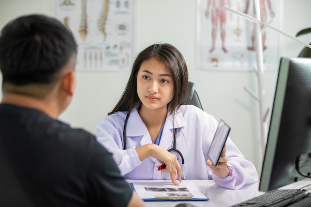 Asiatische Frauen Arzt- und Mannpatientendiskussion über Ergebnisröntgenbilder im Klinikbüro