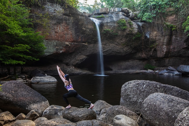 Asiatische frauen des jungen mädchens spielt yoga vor dem wasserfall