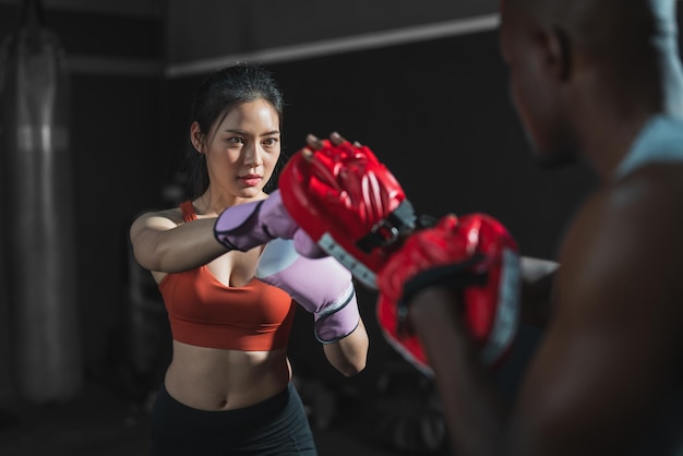 Asiatische Frauen, die Boxhandschuhe mit ihrem Trainertraining und Übungsboxen im Fitnessstudio tragen.