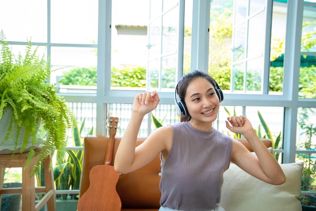 Asiatische Frauen, die Kopfhörer tragen und Laptop und digitales Tablet verwenden, um an einem entspannten Tag Musik zu hören und zu singen und zu Hause Kaffee zu trinken