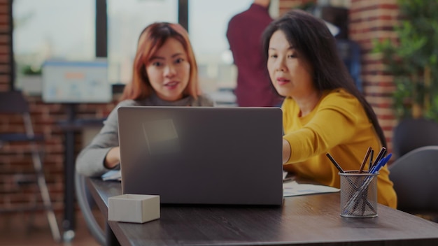 Asiatische Frauen, die Laptop verwenden, um Geschäftsprojekt im Büro zu erforschen. Arbeitskollegen, die Computer betrachten, um die Verbindung mit einer erfolgreichen Organisation für das Wachstum und die Entwicklung des Unternehmens zu planen.