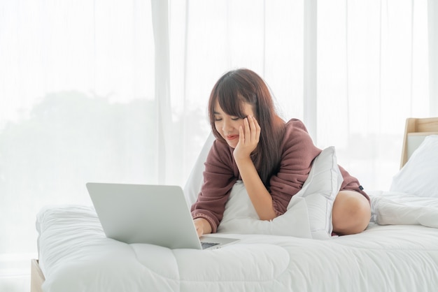 Asiatische Frauen, die mit Laptop auf Bett zu Hause arbeiten