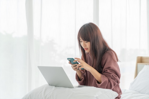 Asiatische Frauen, die mit Laptop auf Bett zu Hause arbeiten