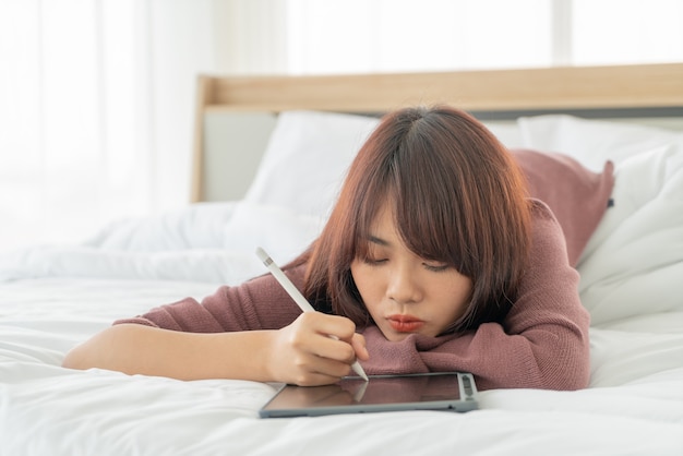 Asiatische Frauen, die mit Tablette auf Bett arbeiten