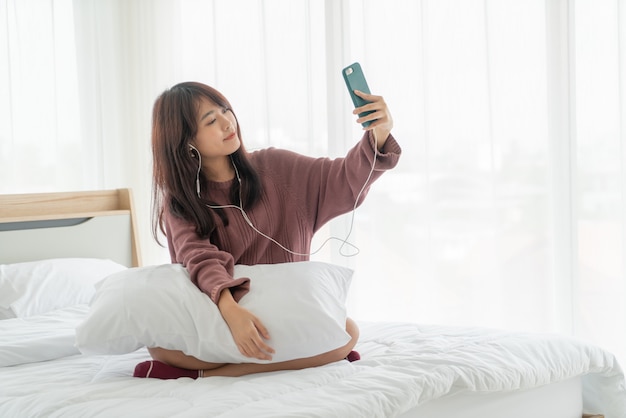 Asiatische Frauen, die Smartphone auf Bett spielen