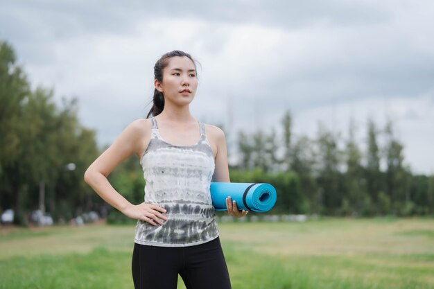 Asiatische Frauen, die Yogamatten halten, werden im Park Yoga machen, um gesund zu bleiben und eine gute Form zu haben.