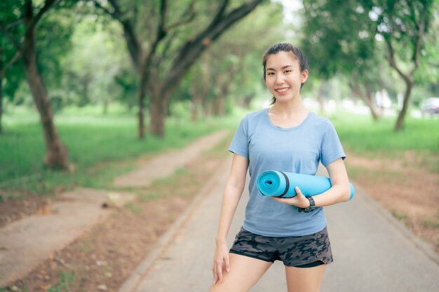 Asiatische Frauen, die Yogamatten halten, werden im Park Yoga machen, um gesund zu bleiben und eine gute Form zu haben.