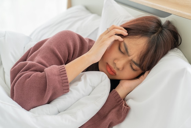 Asiatische Frauen Kopfschmerzen und Schlafen auf dem Bett
