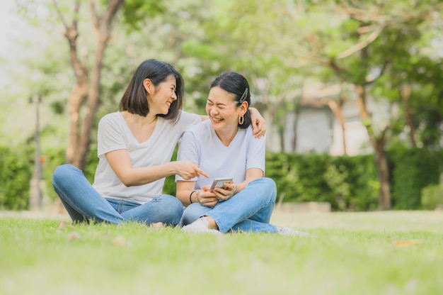 Asiatische Frauen lachen, während sie Smartphone im Freien benutzen