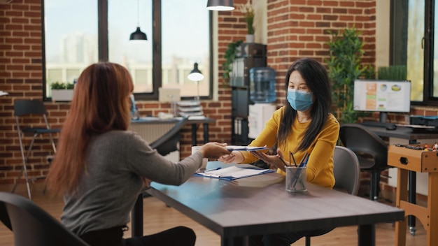 Asiatische Frauen mit Gesichtsmaske treffen sich bei Bewerbungsgesprächen im Startup-Büro. Kandidat nimmt an Einstellungstermin mit Geschäftsfrau teil, um über Rekrutierung und Unternehmen zu sprechen.