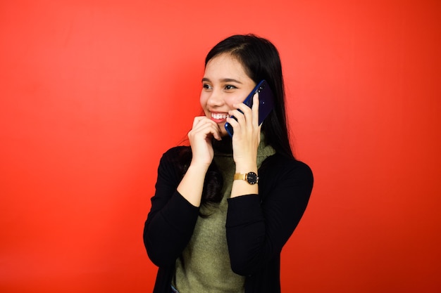 asiatische Frauen mit schwarzem Pullover lächeln und sprechen auf dem Handy mit rotem isoliertem Hintergrund