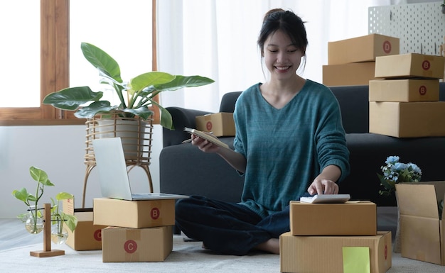 Asiatische Frauen schreiben eine Notiz von Warenbestellungen mit einem lächelnden Gesicht im Konzept des KMU-E-Commerce-Geschäfts