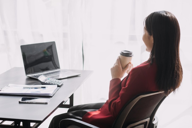 Asiatische Frauen sind gestresst, während sie am Laptop arbeiten Müde asiatische Geschäftsfrau mit Kopfschmerzen im Büro, die sich am Arbeitsplatz krank fühlt