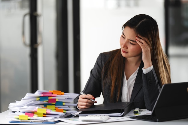 Asiatische Frauen sind gestresst, während sie an Dokumenten in der Hand arbeiten Müde asiatische Geschäftsfrau mit Kopfschmerzen im Büro, die sich bei der Arbeit krank fühlt