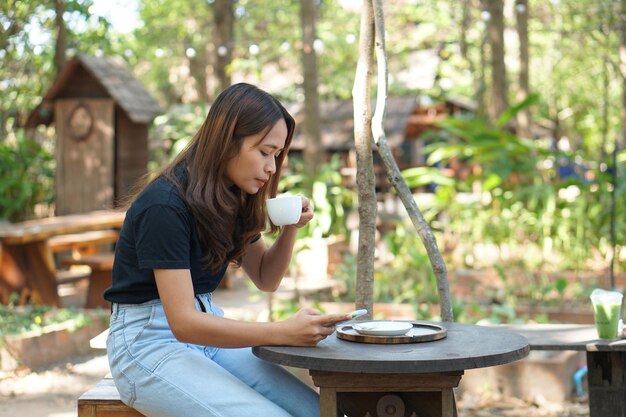 Asiatische Frauen sitzen und arbeiten gerne in einem Café. Es gibt grüne Bäume, umgeben von Natur. Geschäftsplanung ist eine gute Idee