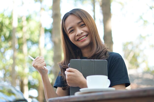 Asiatische Frauen sitzen und arbeiten gerne in einem Café. Es gibt grüne Bäume, umgeben von Natur