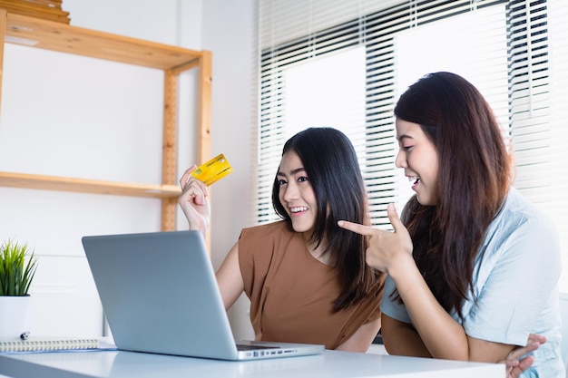 Asiatische Frauen und ihre Freundin Verwenden von Kreditkarten zum Spaß beim Online-Shopping