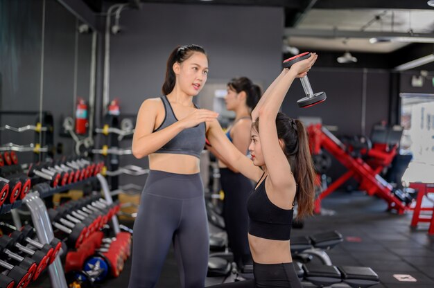 Asiatische Frauenübung und Lebensstil im Fitness-Studio. Sportliches Frauentraining mit Trainer und Hantelgewicht. Wellness und gesund für Bodybuilding.