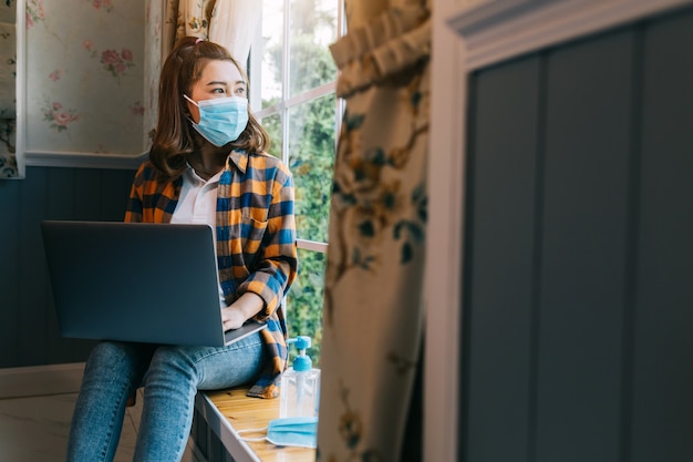 Asiatische Freiberuflerinnen tragen eine Maske, die an einem Projekt arbeitet, bei dem Internetforscher Daten mit einem Laptop analysieren