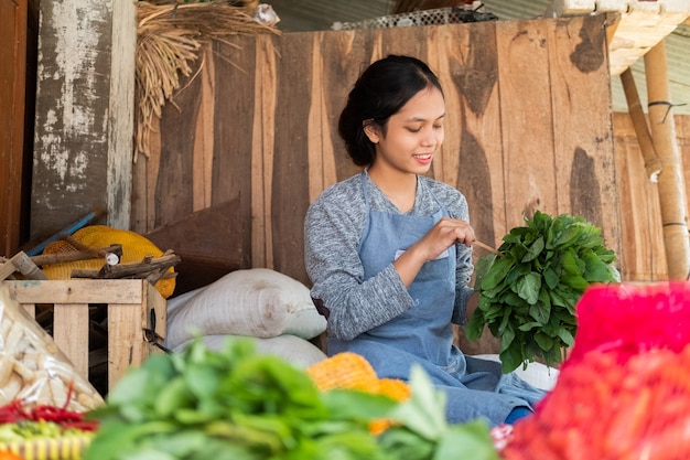 Asiatische Gemüsehändlerin, die Spinat hält, um im Gemüsestand zu binden