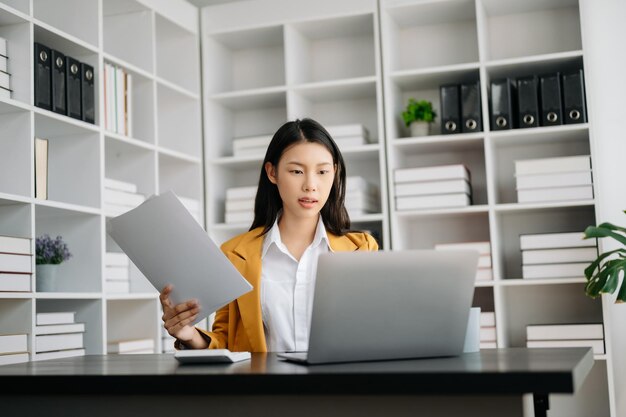 Asiatische Geschäftsfrau arbeitet im Büro mit einem Arbeitsblatt, Tablet und Laptop-Dokumenten