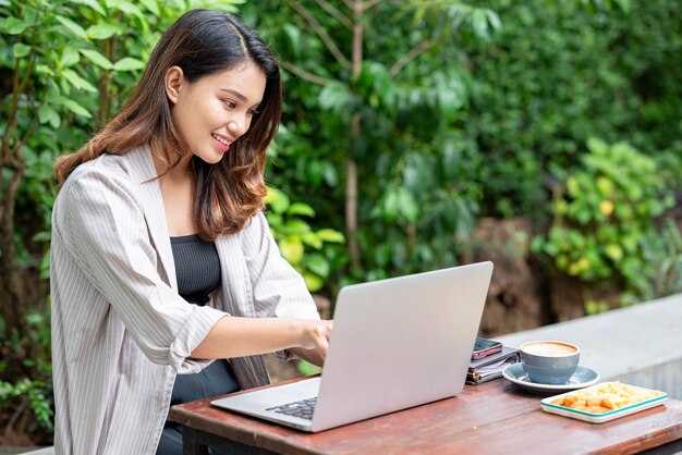 Asiatische Geschäftsfrau benutzt einen Laptop mit einem Mobiltelefon-Notebook und einer Tasse Kaffee auf dem Tisch