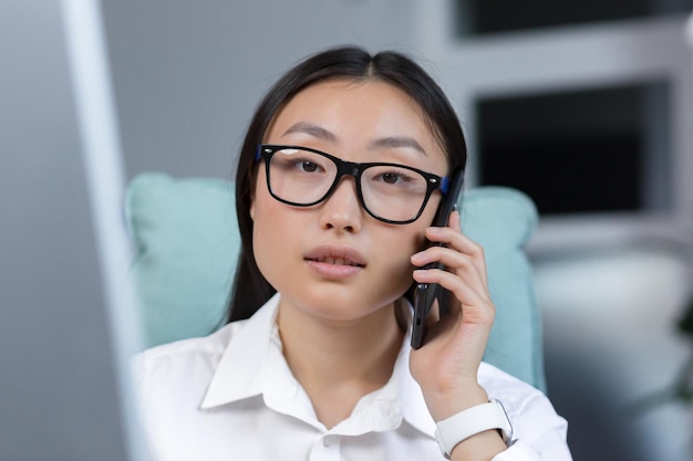 Asiatische Geschäftsfrau des Fotonahaufnahmeporträts, die am Telefon spricht junger Büroangestellter bei der Arbeit