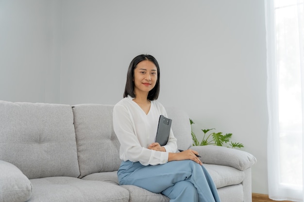 Asiatische Geschäftsfrau, die ein Buch im Büro lächelt und hält Schöne und gut aussehende asiatische Frau sitzt auf dem Sofa weibliche Porträts