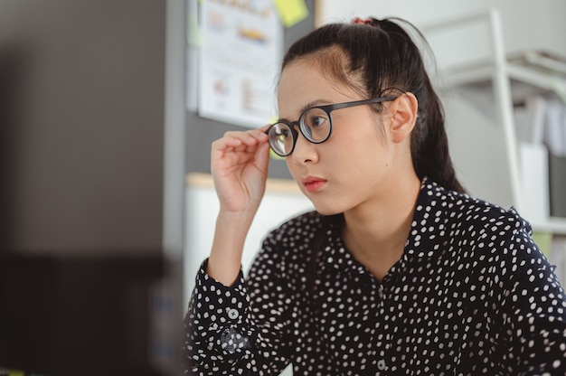 Asiatische Geschäftsfrau, die eine Brille arbeitet und hält, die sich auf das Computergeschäft konzentriert und online arbeitet