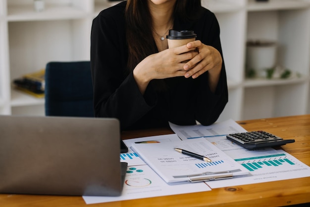 Asiatische Geschäftsfrau, die einen Laptop-Computer verwendet und im Büro mit einem Taschenrechnerdokument auf dem Schreibtisch arbeitet, um die Analyse des Finanzberichts-Geschäftsplan-Investitionsfinanzierungsanalysekonzepts zu planen