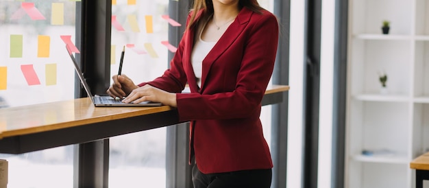 Asiatische Geschäftsfrau, die einen Laptop-Computer verwendet und im Büro mit einem Taschenrechnerdokument auf dem Schreibtisch arbeitet, um die Analyse des Finanzberichts-Geschäftsplan-Investitionsfinanzierungsanalysekonzepts zu planen