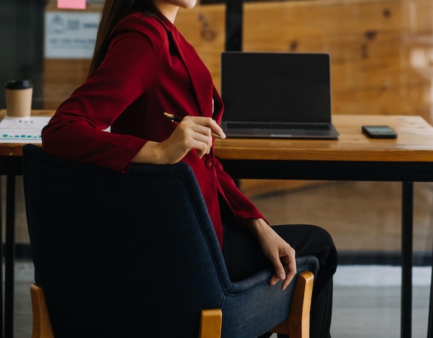 Asiatische Geschäftsfrau, die einen Laptop-Computer verwendet und im Büro mit einem Taschenrechnerdokument auf dem Schreibtisch arbeitet, um die Analyse des Finanzberichts-Geschäftsplan-Investitionsfinanzierungsanalysekonzepts zu planen