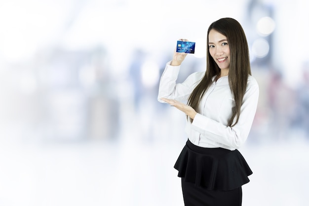 Asiatische Geschäftsfrau, die Kreditkarte auf unscharfem Hintergrund zeigt.