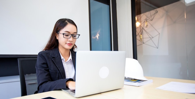 Asiatische Geschäftsfrau, die Laptop für die Arbeit verwendet und Internetrecherchen in ihrem Büro durchführt