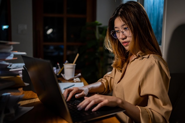 Asiatische Geschäftsfrau, die nachts online arbeitet. Beschäftigt und erschöpft von Überstunden zu Hause