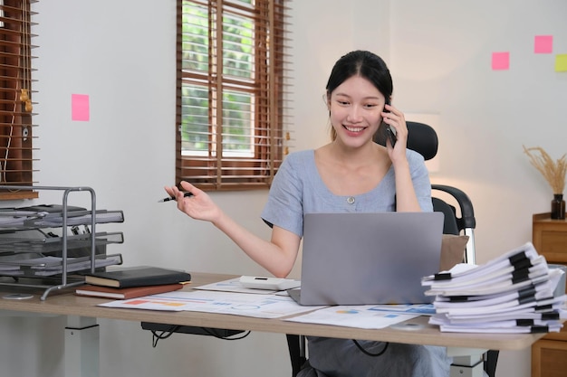 Asiatische geschäftsfrau, die smartphone verwendet, um mathefinanzierung auf hölzernem schreibtisch im finanzkonzept der bürosteuerbuchhaltung zu tun